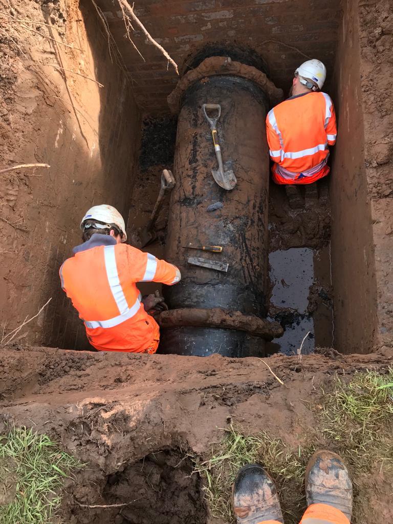 A section of ductile iron pipe leaking from two coupling joints in a pipe pit prior to undergoing a live leak repair