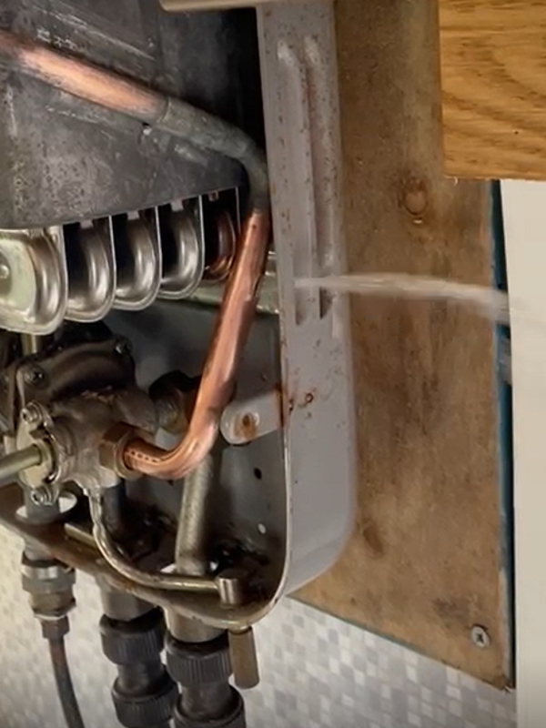 A pressurised jet of water escaping from a copper pipe in a camper van boiler system prior to undergoing repair