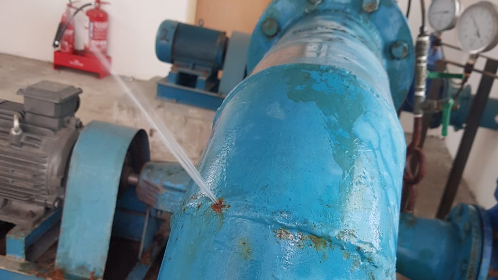 A pinhole leak in a 150mm steel elbow joint prior to undergoing repair using a SylWrap Pipe Repair Kit