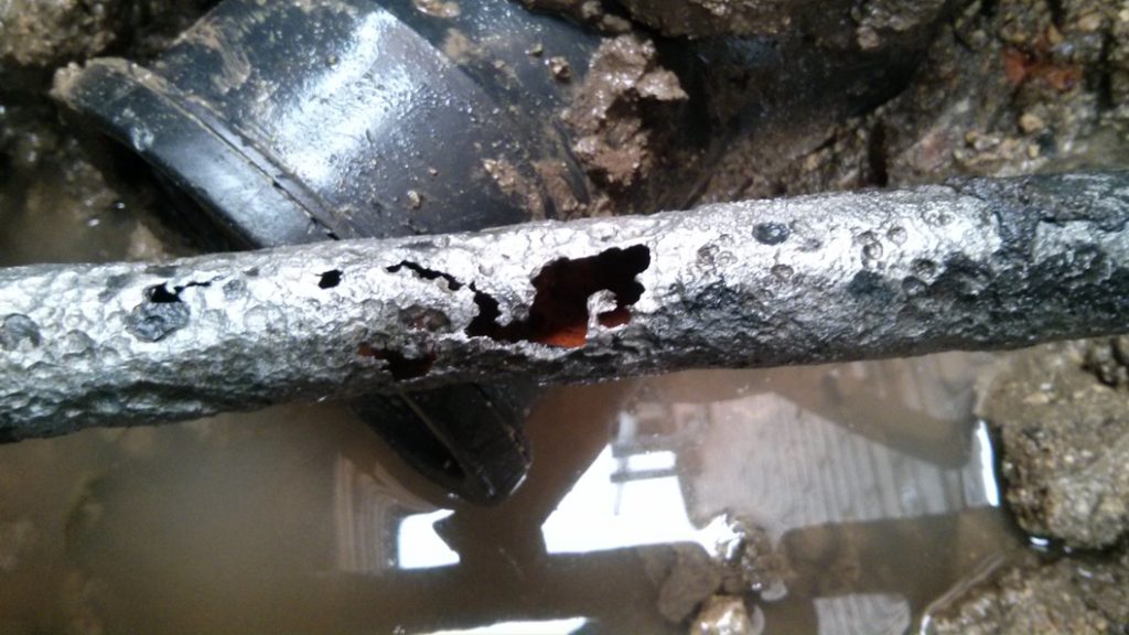 A crack in a 90-year-old malleable iron water supply pipe caused by corrosion prior to undergoing repair with a SylWrap Standard Pipe Repair Kit