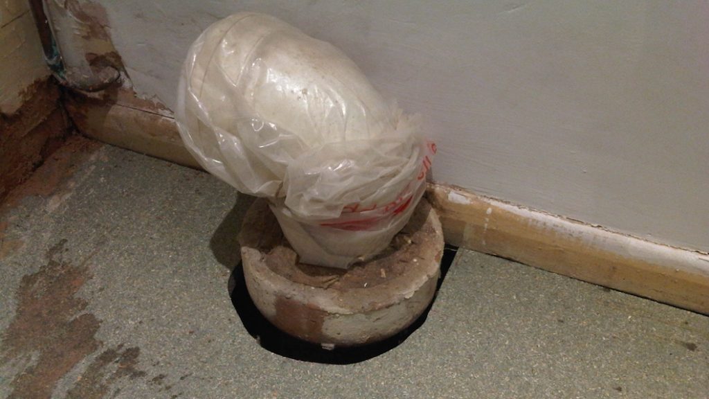 A toilet waste pipe suffering a crack between the base and a bathroom floor before being repaired with Sylmasta AB Epoxy Putty