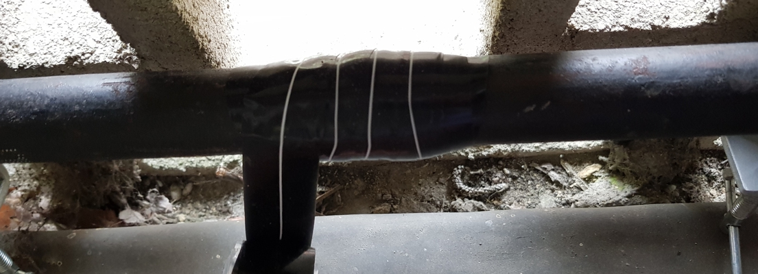 A malleable iron water supply pipe in a restricted space undergoes repair using Wrap & Seal Pipe Burst Tape