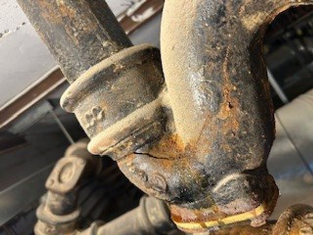 Crack across a cast iron waste pipe U-bend before repair at an NHS hospital in the UK